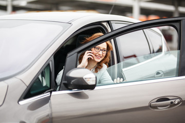Fototapeta na wymiar Attractive red hair businesswoman getting out of car and talking on phone.