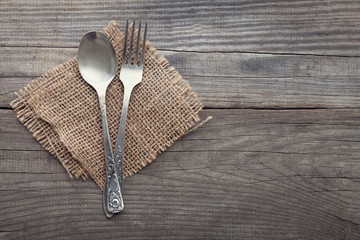 Old fork and spoon on a wooden table napkin and burlap, grunge rustic style, top view.