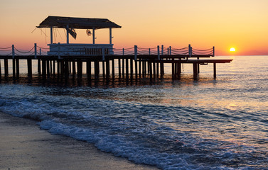 Fototapeta premium altanka na drewnianym molo do morza ze słońcem o zachodzie słońca
