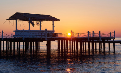 Fototapeta na wymiar gazebo on the wooden pier into the sea with the sun at sunset