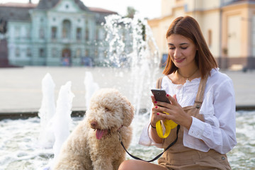 Woman using smart phone and  enjoying summer days with her dog. - obrazy, fototapety, plakaty