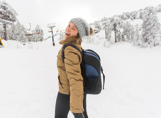 Fototapeta na wymiar Woman winter hiking. Beautiful young caucasian woman enjoying snow dressed in a cheerful winter cap and with a satchel on her back with copyspace.