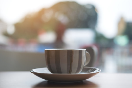 Closeup image of hot coffee cup on wooden table in cafe with blur outdoor background