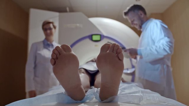 Unrecognizable patient lying in MRI machine and being lifted before procedure as female and male radiologists talking