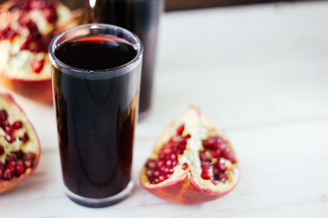 Pomegranate juice in glass surrounded by pomegranate halves.