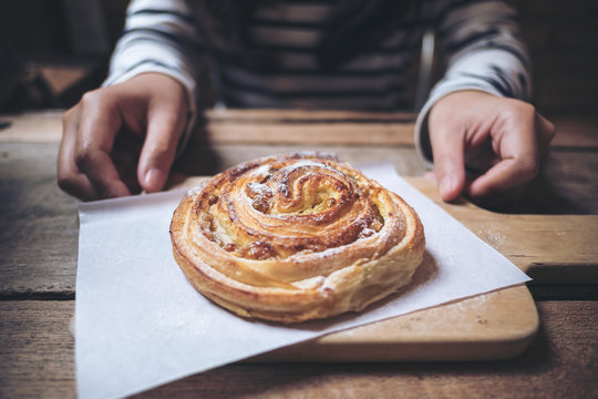 Closeup image of a woman holding and giving a raisin danish on wooden vintage table in bakery shop