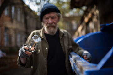 Dirty old tramp looking at empty bottle in his hand. Difficult life of homeless old man.