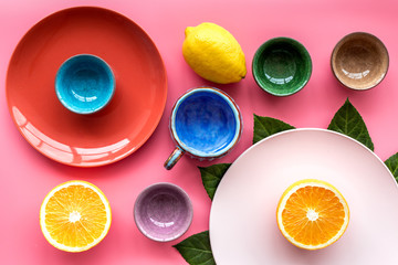 Colored cups and plates pattern decorated by exotic leaves and fruits on pink background top view