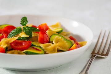 Closeup of whole farfalle pasta with zucchini, cherry tomatoes and red onion