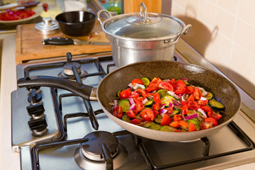 Zucchini, cherry tomatoes and red onion cooking in the pan on the cooker