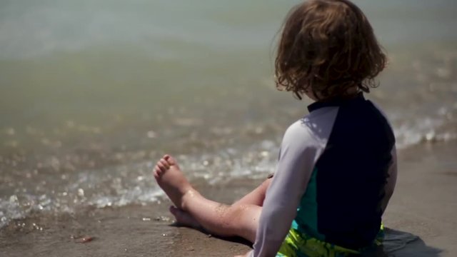 Curious Little Boy Enjoys Looking At Water, Lets Waves Crash On His Legs At Beach, Slow Motion