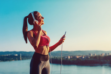 Young woman in sports clothes listen to music via headphones and smartphone