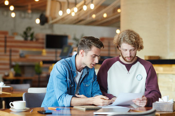 Group of talented financial managers analyzing results of accomplished work while having working meeting at cozy small coffeehouse, blurred background