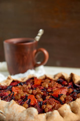 Plums pie with dried apricots close up. On blurred background a cup of tea on brown wooden background. Side view