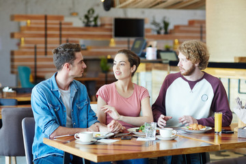 Multi-ethnic group of friends enjoying delicious lunch at cozy small cafe while having long-awaited gathering, lovely interior on background