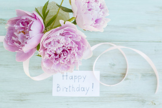 Greeting card, peonies and the inscription "Happy Birthday" on a turquoise background