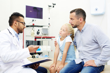 Obraz premium Doctor giving advice for little girl while talking to her father during visit