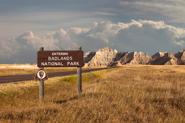 Beautiful landscape of badlands entering wood sign with clouds and large mountain range butte