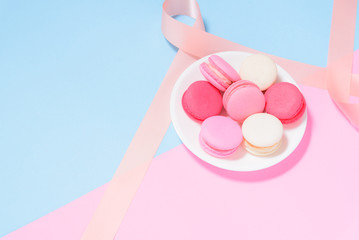 Colorful macaroons or macaron on White plate with pink ribbon on pink and blue pastel background