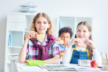 Schoolboy with cracker and his classmate with sandwich having lunch break after lesson
