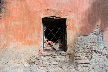 Old broken concrete and brick wall with a window with iron grating