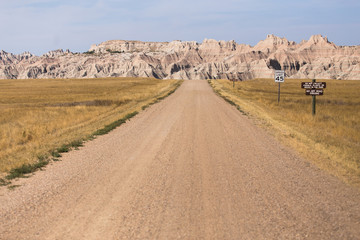 Open dirt road entering badlands national park with mountain range formation in background