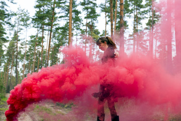 Young woman in forest having fun with red smoke grenade, bomb