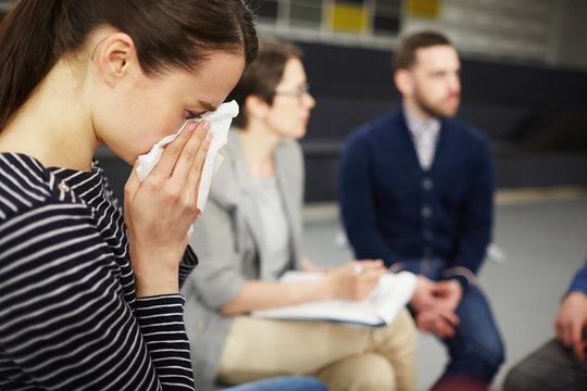 Crying woman wiping her tears with handkerchief with groupmates communicating on background