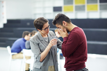 Young man grieving and crying while helpful woman comforting him and offering glass of water