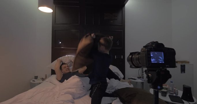 Fixed on tripod camera taking video of dad and son fighting with pillows in bedroom. Fun and leisure of parents and children