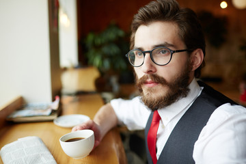 Bearded man in eyeglasses and elegant formalwear having five oclock tea