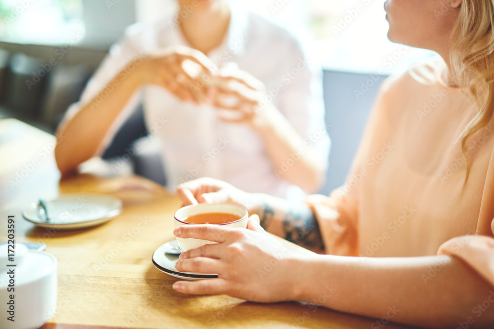 Poster young friendly girls having tea and talk in cafeteria on weekend