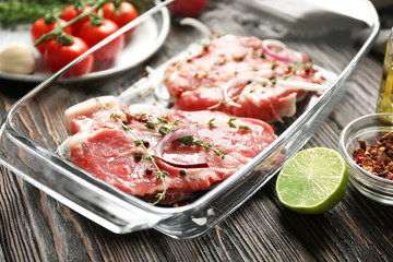 Baking dish with fresh raw steaks on table