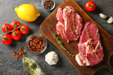 Composition with fresh raw steaks, thyme and vegetables on table