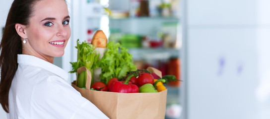 Young woman holding grocery shopping bag with vegetables .Standing in the kitchen. Woman in the kitchen looking at the camera