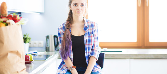 Portrait of young woman standing with arms crossed against kitchen background.