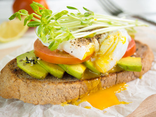 Poached egg,tomato and avocado on whole wheat toast topping with bean sprouts for healthy breakfast.
