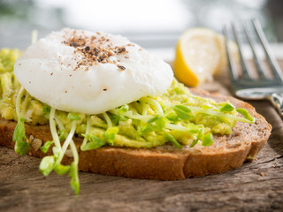 Poached egg and mashed avocado on whole wheat toast for healthy breakfast.
