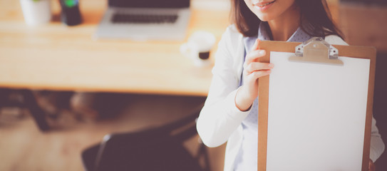 Young woman standing near desk with laptop holding folder and cup of coffee. Workplace. Business...
