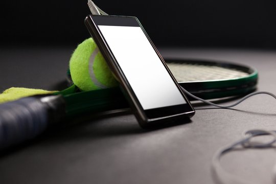 Close up of mobile phone and headphones by tennis ball with