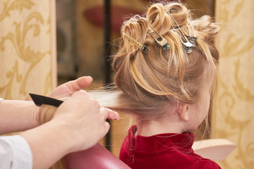Little girl getting hair done. Hands of hairstylist working.