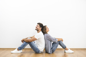 The smile man and woman sit on the background of the empty wall - obrazy, fototapety, plakaty