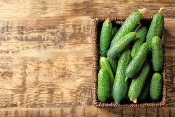 Many green fresh cucumbers in wicker basket on wooden table