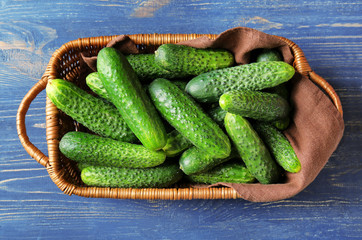 Many green fresh cucumbers in wicker basket on wooden table