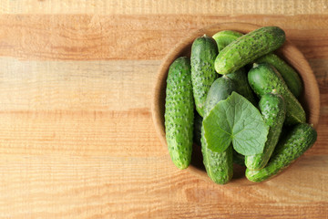 Green fresh cucumbers in bowl on wooden table