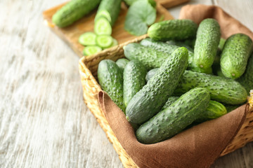 Many green fresh cucumbers in wicker basket on wooden table
