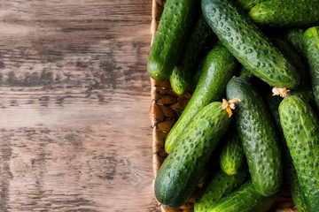 Many green fresh cucumbers in wicker basket on wooden table