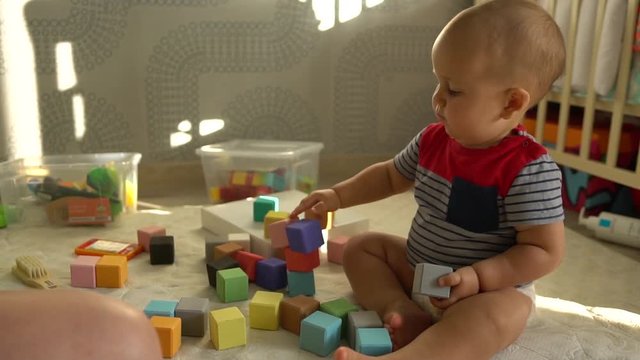 Cute toddler boy plays with colorful baby blocks sitting on a floor. Slow motion shot