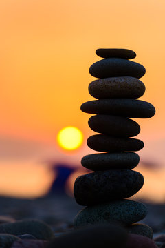 Stones pyramid on sand symbolizing zen, harmony, balance. Black sea at sunset in the background.