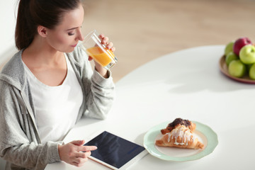 Young woman with orange juice and tablet in kitchen.